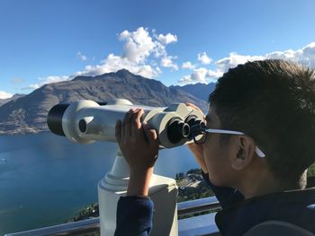 Close-up of boy looking through coin-operated binoculars against valley