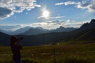 Woman photographing sun shining through mountains