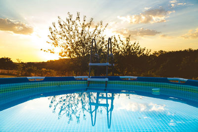 Chairs by swimming pool against sky at sunset