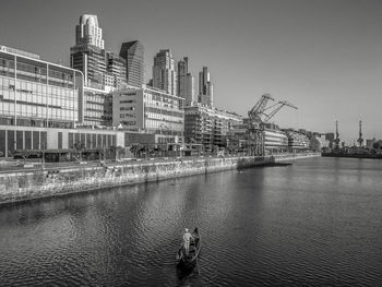 Man in boat on river by city against clear sky