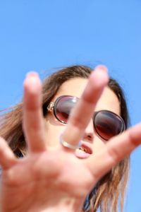 Low angle portrait of young woman showing stop gesture against clear blue sky