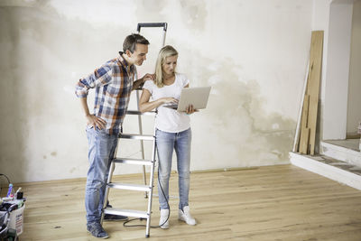 Woman using laptop while standing by boyfriend at home during renovation