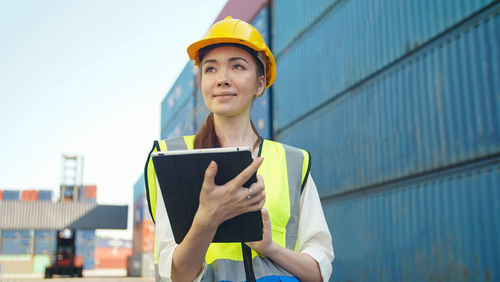 Portrait of young woman using digital tablet while standing against wall