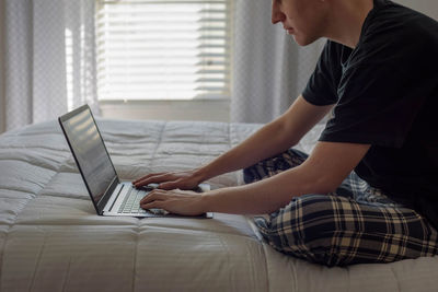 Midsection of man using laptop while sitting on bed at home