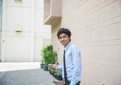 Young man using smart phone while standing against wall