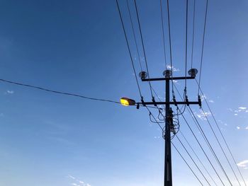 Low angle view of electricity pylon against blue sky