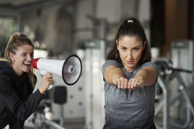 Fitness instructor with megaphone assisting woman in exercising at gym