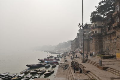 Boats moored at port in city against sky