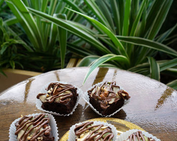 Chocolate brownie cubes with chocolate drizzle in paper cups on a wooden background.