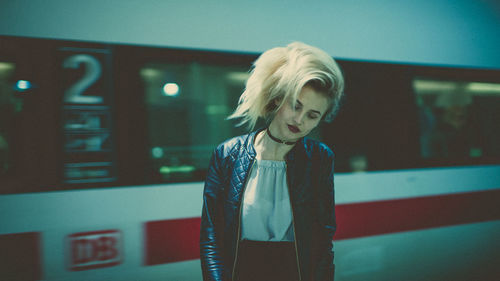 Portrait of young woman standing against wall at night