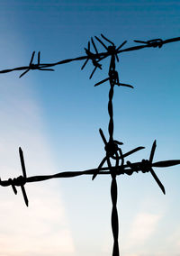 Barbed wire fence against cloudy sky during sunset