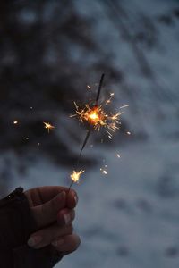 Cropped hand of woman holding illuminated sparkler at night