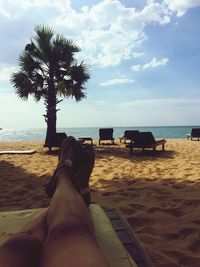 Low section of man sitting on beach against sky