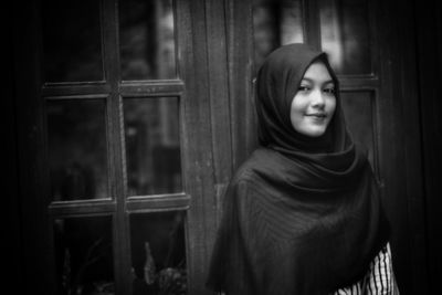 Portrait of smiling woman standing against window