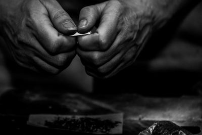 Cropped hands of man making marijuana joint on floor