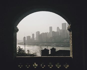 Silhouette buildings by river against sky seen through arch