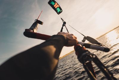 Cropped hands of man kiteboarding in sea against sky