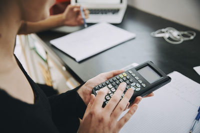 Midsection of young female student using calculator in classroom at university