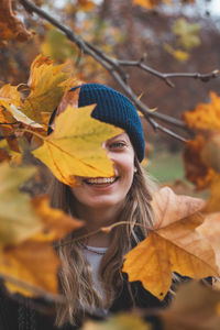 Smiling brunette in a blue knitted hat enjoying the autumn colours in an oak forest.
