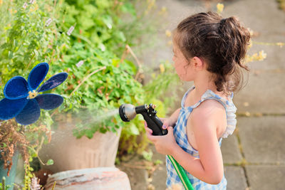 Young girl is watering plants in the backyard while wearing a bathing suit