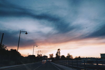Cars on road against dramatic sky during sunset