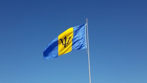 Low angle view of barbados flag against blue sky