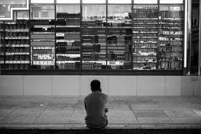 Rear view of man sitting at sidewalk in city