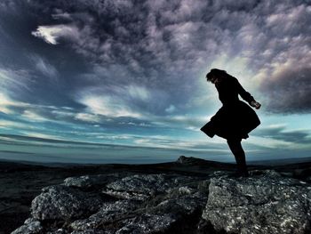 Man standing on rocks against cloudy sky