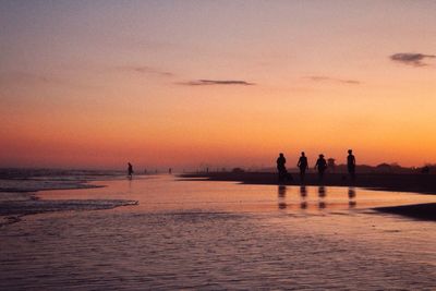 Silhouette people on sea against sky at sunset