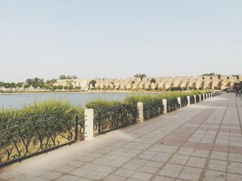 Footpath by railing in city against clear sky