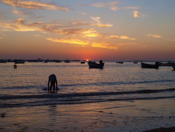 Silhouette man standing in sea against sky during sunset