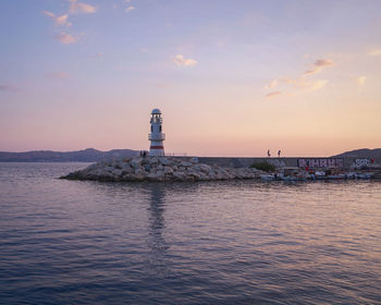 Lighthouse by sea against sky during sunset