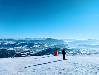 Man skiing on snow covered land against sky during winter