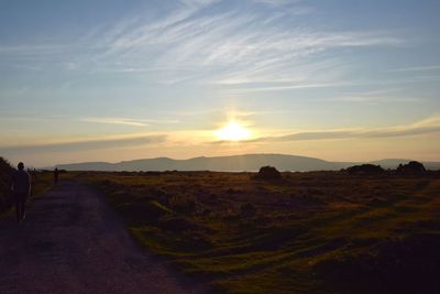 Rear view of silhouette woman walking on landscape against sky during sunset
