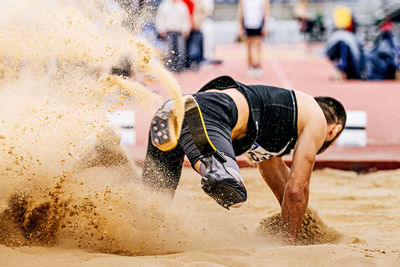 Rear view of man playing with sand at beach