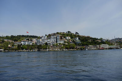 Sea by buildings in town against sky