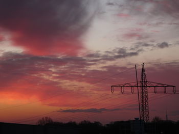 Low angle view of silhouette electricity pylon against dramatic sky