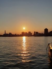 Silhouette buildings by sea against clear sky during sunset