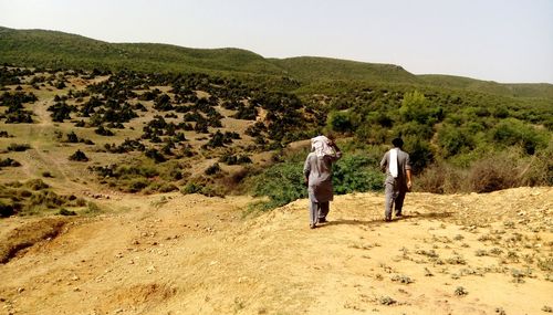 Rear view of men walking on dirt road against sky