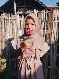 Portrait of woman with pink umbrella standing against wood