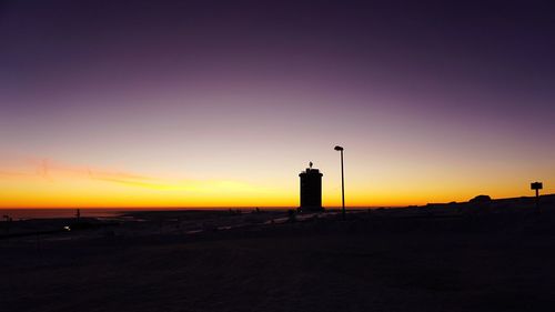 Silhouette of lighthouse at beach during sunset