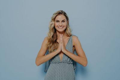 Portrait of young woman standing against blue background