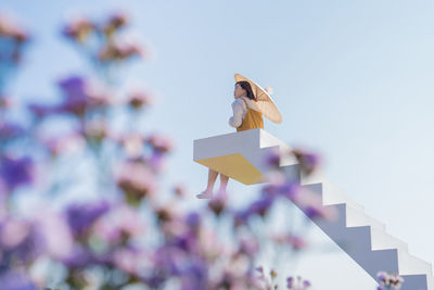 Low angle view of woman with umbrella sitting on steps against sky