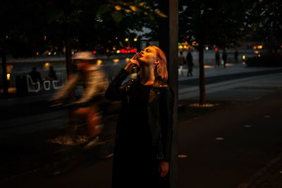 Woman smoking cigarette in city at night