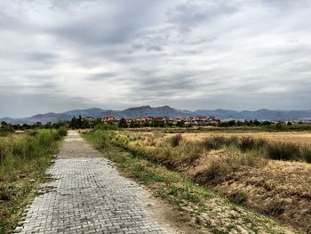 Footpath passing through landscape against cloudy sky