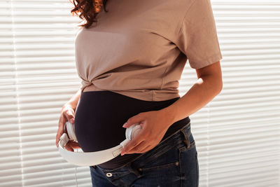 Midsection of pregnant woman holding headphones