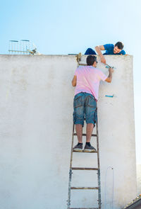 Rear view of people on wall against sky