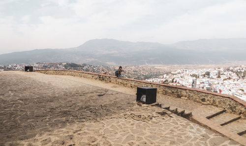 Woman sitting on retailing wall against town and mountains