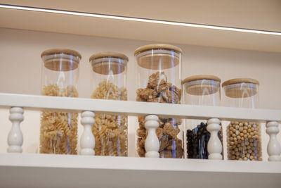 Glass jars of macaroni, nuts and grains on a kitchen shelf