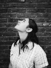 Young woman looking up against brick wall